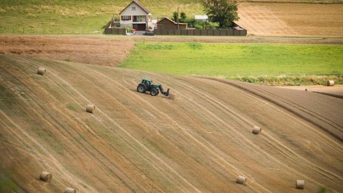 Champ de cultures avec une ferme, un tracteur et des ballots de paille.